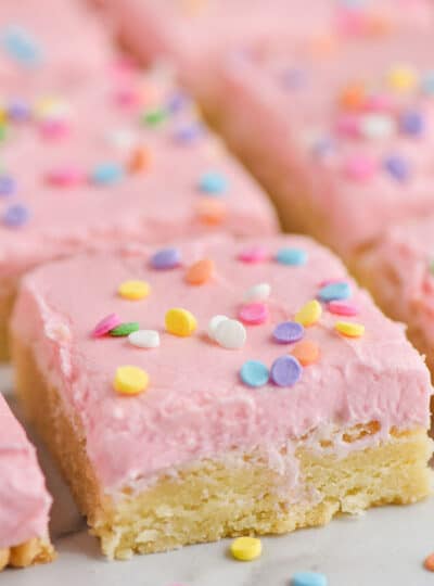 close up of a sugar cookie bar with pink buttercream frosting and circle pastel sprinkles on a white surface