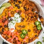 overhead view of an easy taco casserole recipe in a skillet, being spooned out, you can see beans, meat, rice, and corn - 9