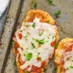 overhead view of a piece of oven baked chicken parmesan on an old tray garnished with fresh parsley