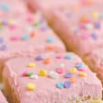 close up of a sugar cookie bar with pink buttercream frosting and circle pastel sprinkles on a white surface