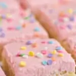 close up of a sugar cookie bar with pink buttercream frosting and circle pastel sprinkles on a white surface