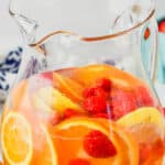 a pitcher of white sangria with slices of oranges, fresh raspberries and other fruit in it