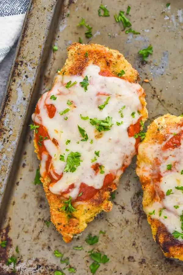 overhead view of a piece of oven baked chicken parmesan on an old tray garnished with fresh parsley