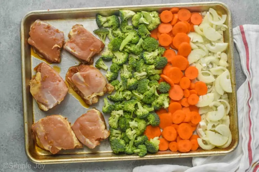 a sheet pan with chicken thighs, broccoli, carrots, and onions before being baked