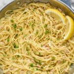 overhead photo of linguine with clams in a large skillet, garnished with fresh parsley and two lemon wedges
