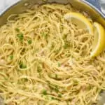 overhead photo of linguine with clams in a large skillet, garnished with fresh parsley and two lemon wedges