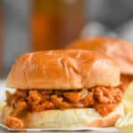 a turkey sloppy Joe on a white bun sitting on an overturned rimmed metal baking sheet with ruffled potato chips around it