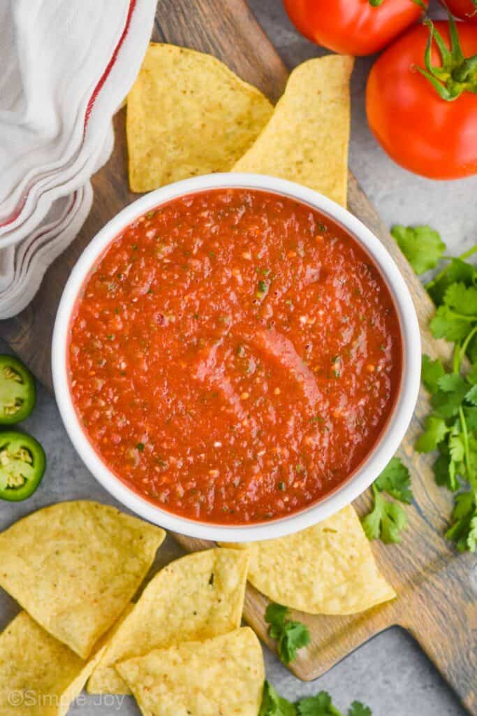 overhead view of easy salsa recipe in a white bowl on a cutting board surrounded by tortilla chips, cilantro, and tomatoes