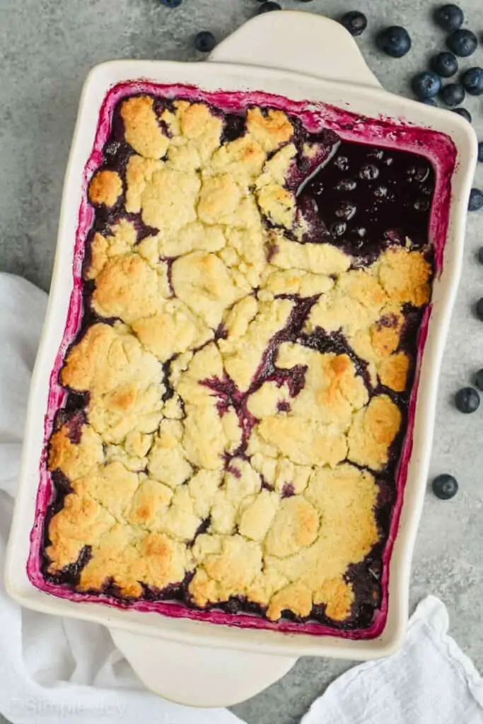 pulled back overhead view of ceramic dish full of blueberry cobbler recipe with one piece missing