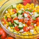 close up of corn salad in a glass bowl with fresh cut cucumbers, tomatoes, red onions, feta cheese, and fresh basil on top - 19