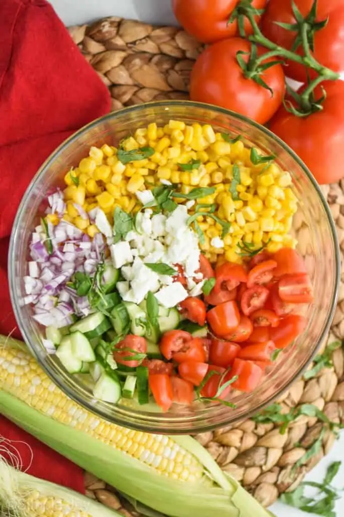 overhead view of a glass bowl full of the ingredients for corn salad recipe divided up