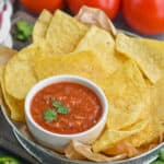 a small white bowl of salsa recipe garnished with cilantro in a metal tin with tortilla chips