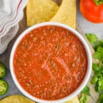 overhead view of easy salsa recipe in a white bowl on a cutting board surrounded by tortilla chips, cilantro, and tomatoes