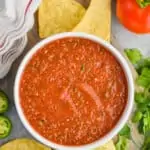 overhead view of easy salsa recipe in a white bowl on a cutting board surrounded by tortilla chips, cilantro, and tomatoes