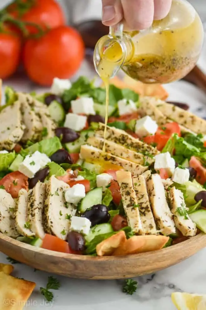 greek salad dressing being poured onto a greek salad with chicken