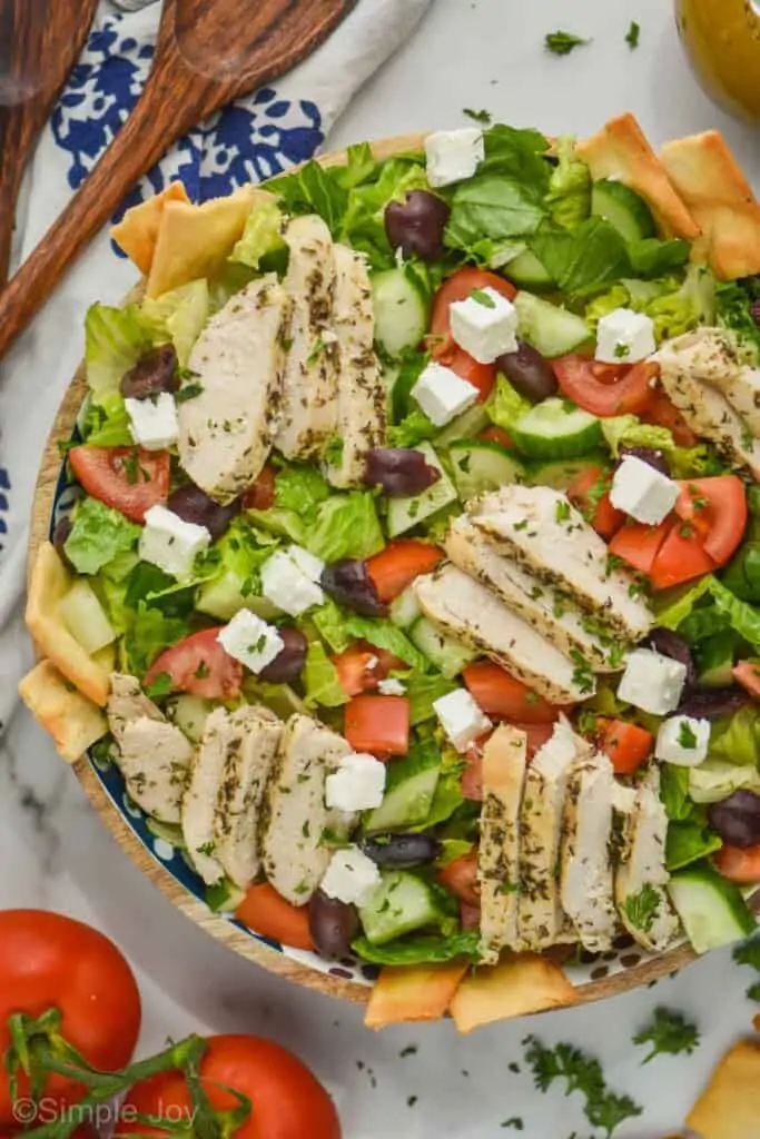 overhead view of a greek salad with chicken, with pita chips sticking out around the edges of the bowl and garnished with fresh parsley