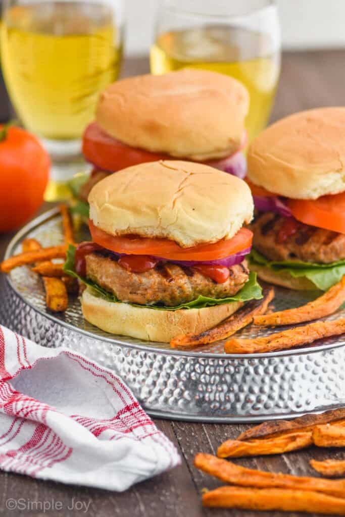 three easy turkey burgers on a silver tray with tomatoes, lettuce, red onions, and ketchup, surrounded by sweet potato fries