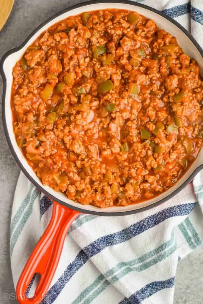 overhead view of turkey sloppy Joe recipe in a skillet that has a black rim and a white inside with a red handle sitting on a blue and white stripped napkin