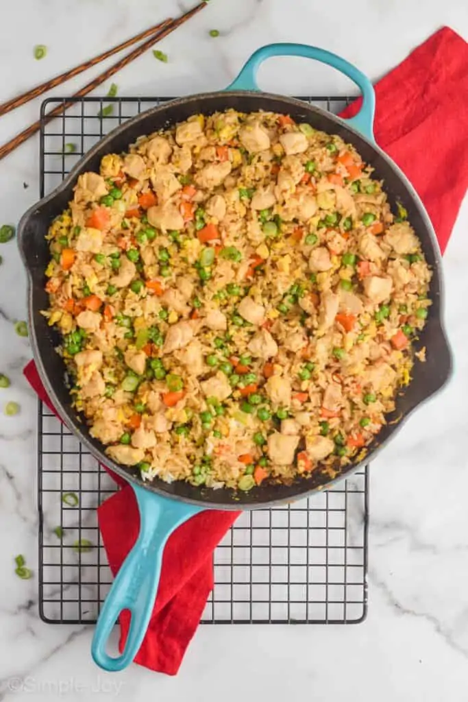 overhead view of a teal skillet filled with chicken fried rice on a wire cooling rack with a red cloth napkin on a white marble surface