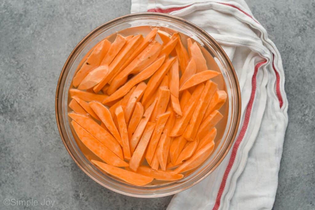 uncooked cut sweet potatoes soaking in a bowl of water