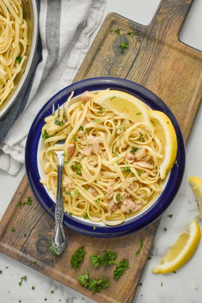 overhead view of a small plate of clam linguine recipe twisted up in a fork, garnished with fresh parsley and with two lemon wedges