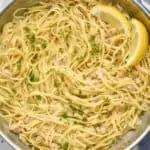 overhead photo of linguine with clams in a large skillet, garnished with fresh parsley and two lemon wedges