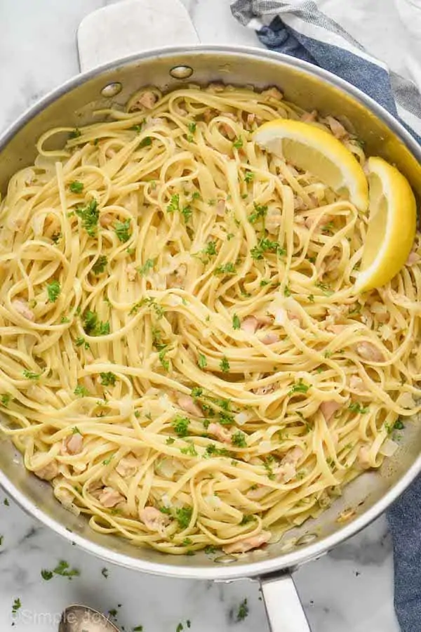 overhead photo of linguine with clams in a large skillet, garnished with fresh parsley and two lemon wedges