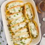 overhead view of a ceramic baking dish filled with 10 baked tacos that have white cheese melted on top, two beer mugs next to the casserole dish - 6
