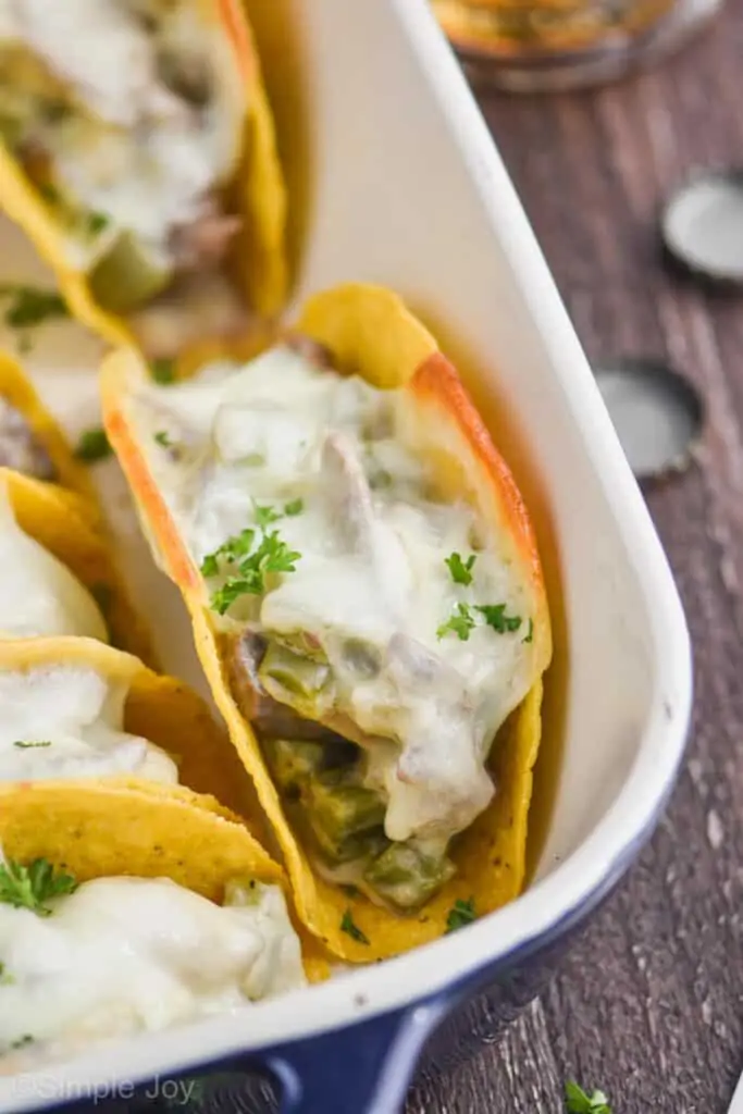 close up of a baked taco in a casserole dish with provolone melted on top and steak and peppers visible in the hard taco shell