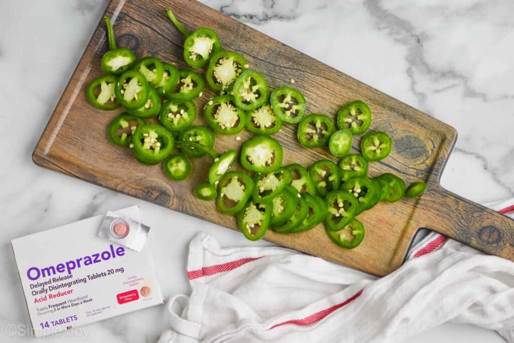 a cutting board with slices of jalapeños next to a box of omeprazole