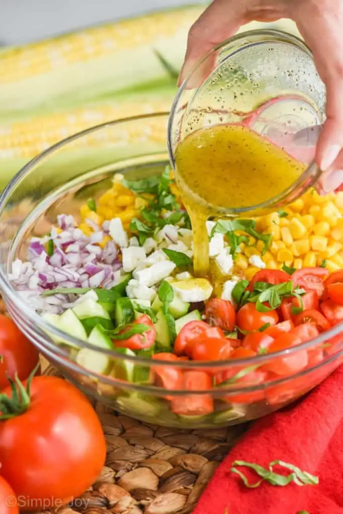 hand pouring dressing over summer corn salad in a glass bowl