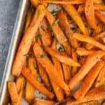 overhead photo of baked sweet potato fries on a baking sheet garnished with fresh parsley