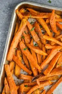 overhead photo of baked sweet potato fries on a baking sheet garnished with fresh parsley