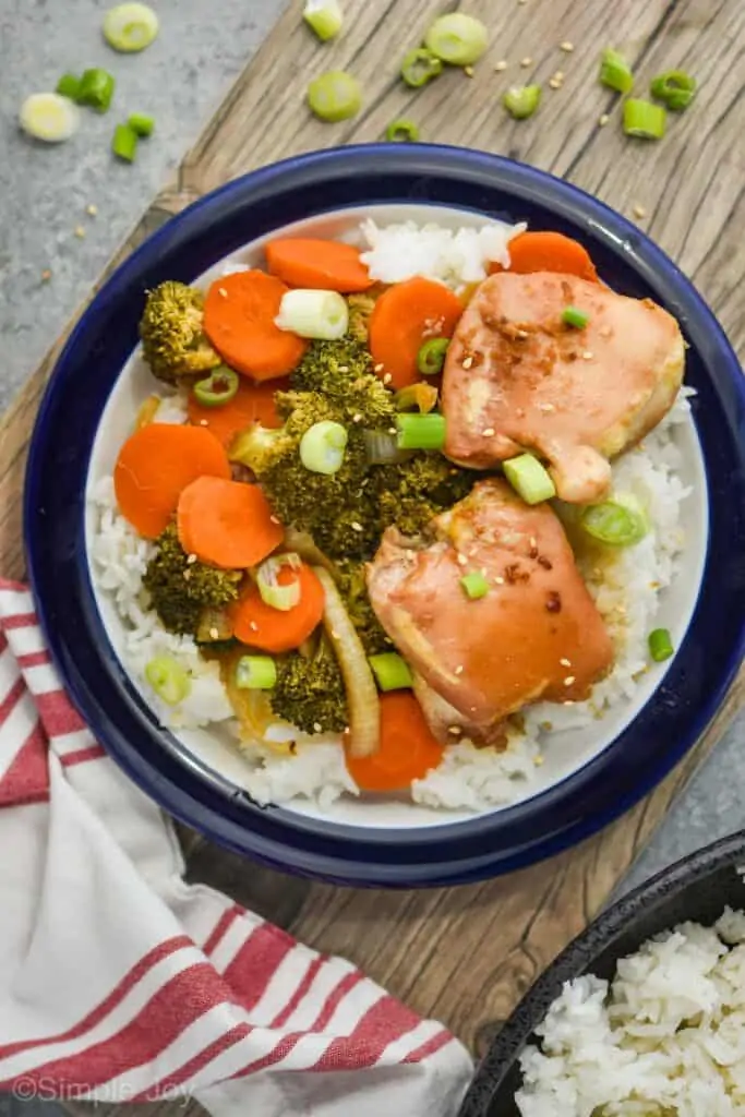 overhead view of a plate of baked teriyaki chicken with vegetables on rice and garnished with fresh green onions