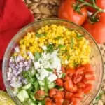 overhead view of a glass bowl full of the ingredients for corn salad recipe divided up