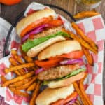 three grilled turkey burgers with lettuce, tomatoes, onions, and ketchup on their sides in a basket, surrounded by sweet potato fries