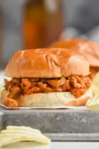 a turkey sloppy Joe on a white bun sitting on an overturned rimmed metal baking sheet with ruffled potato chips around it