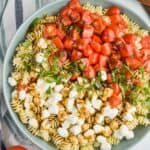 overhead view of a large bowl full of pearl mozzarella, pasta, fresh shredded basil, and quartered cherry tomatoes covered in balsamic dressing - 8