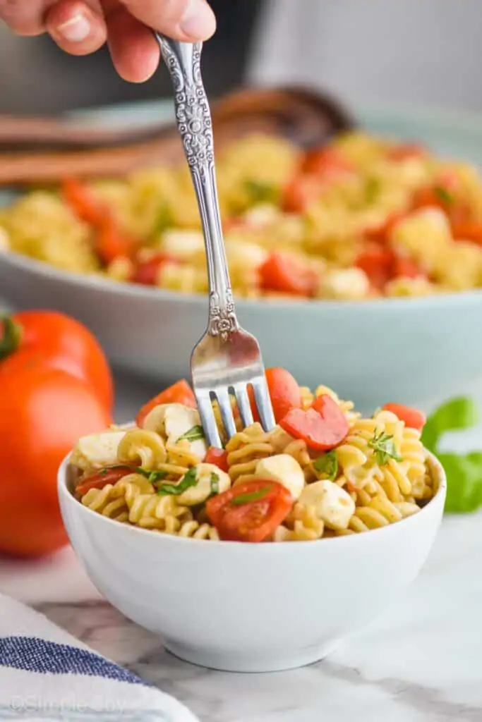 small white bowl full of caprese pasta salad with a fork digging into the middle
