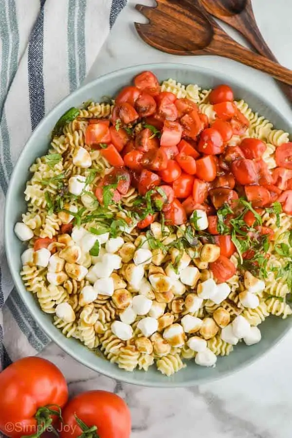 overhead view of a large bowl full of pearl mozzarella, pasta, fresh shredded basil, and quartered cherry tomatoes covered in balsamic dressing