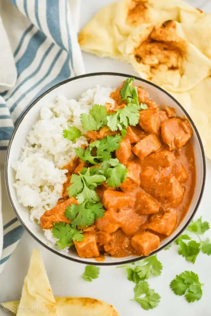 overhead view of a bowl of slow cooker butter chicken on one side of the bowl, rice on the other side, with fresh cilantro down the middle