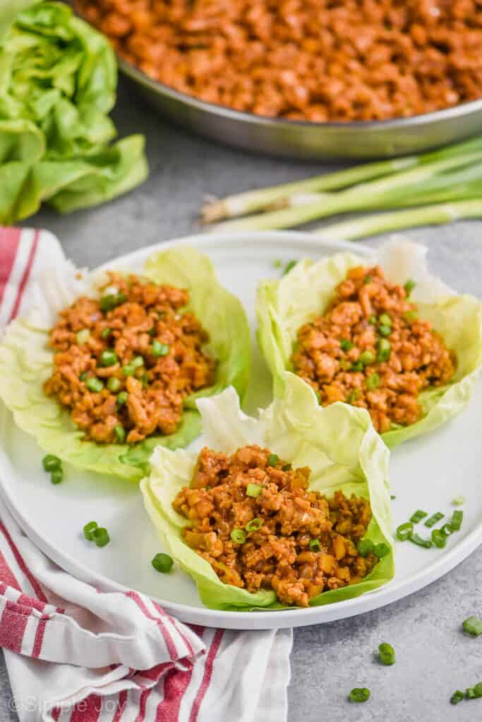 three asian chicken lettuce wraps sitting on a white plate garnished with fresh green onions