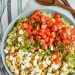 overhead view of a large bowl full of pearl mozzarella, pasta, fresh shredded basil, and quartered cherry tomatoes covered in balsamic dressing