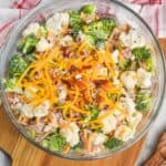 overhead view of broccoli cauliflower salad in a clear serving bowl with extra bacon, cheese, sunflower seeds and red onions on top - 17