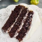 piece of three layer chocolate zucchini cake, frosted with cream cheese on a white plate with two zucchinis in the background - 11