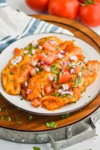 three chicken enchiladas on a plate garnished with cut up cilantro, red onions, and tomatoes