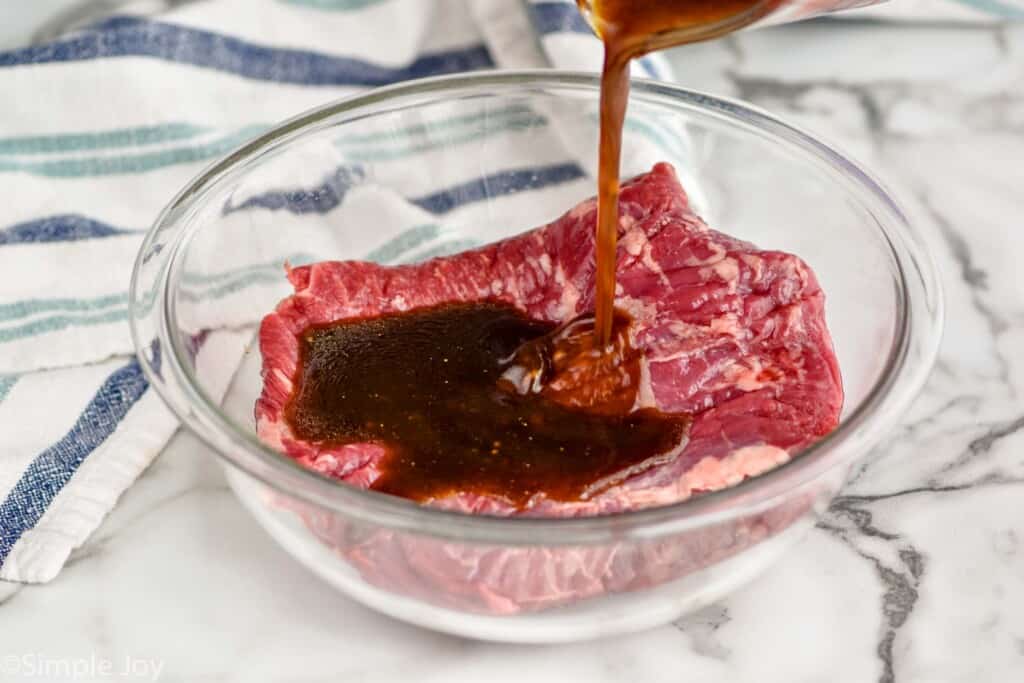 pouring flank steak marinade over a piece of flank steak in a bowl