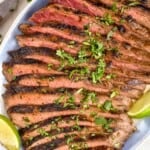 overhead of a grilled flank steak recipe on a platter with cilantro and lime wedges - 11