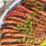 pinterest graphic of overhead of a grilled flank steak recipe on a platter with cilantro and lime wedges