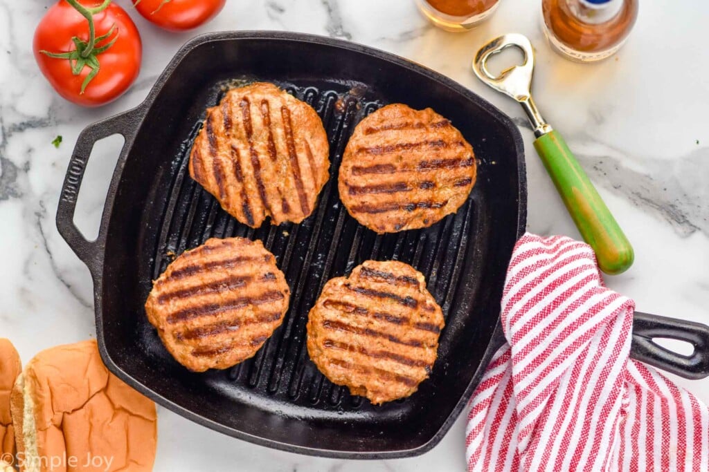 Overhead photo of Turkey Burger recipe in a skillet. Buns, tomatoes, and bottles of beer on counter beside skillet.